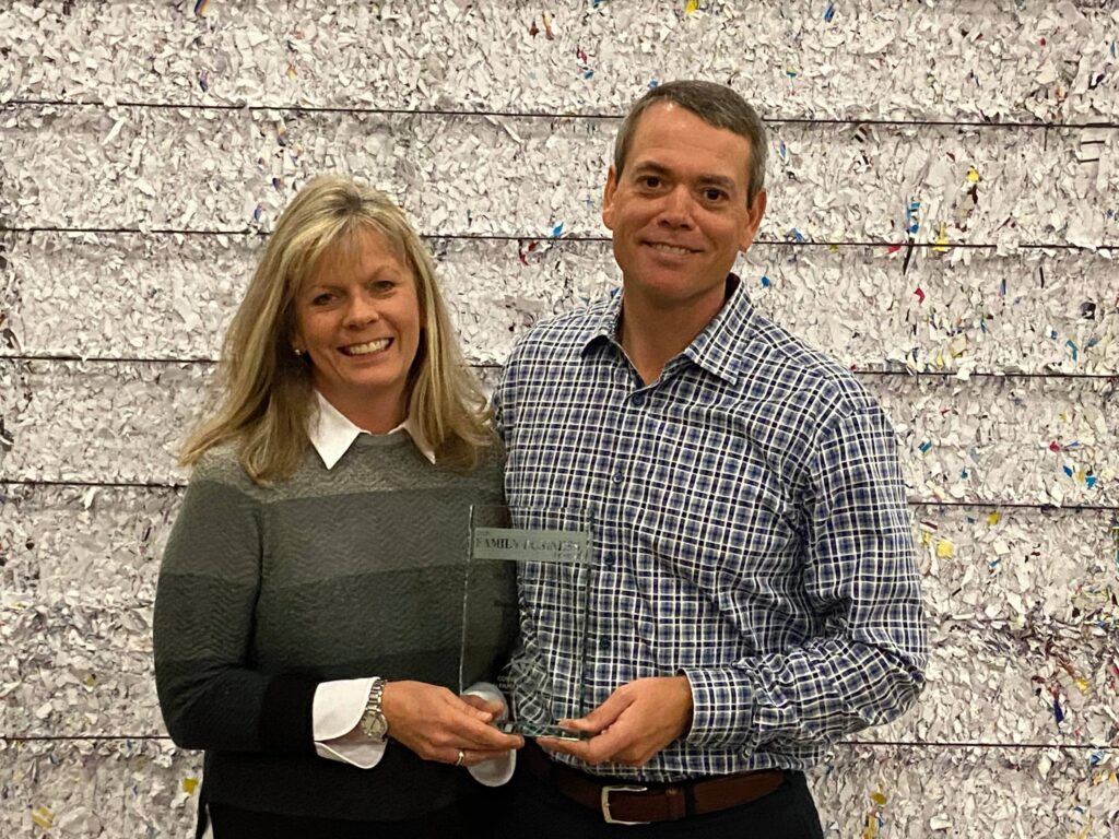 John and Laura Daly holding up award in front of shredded paper