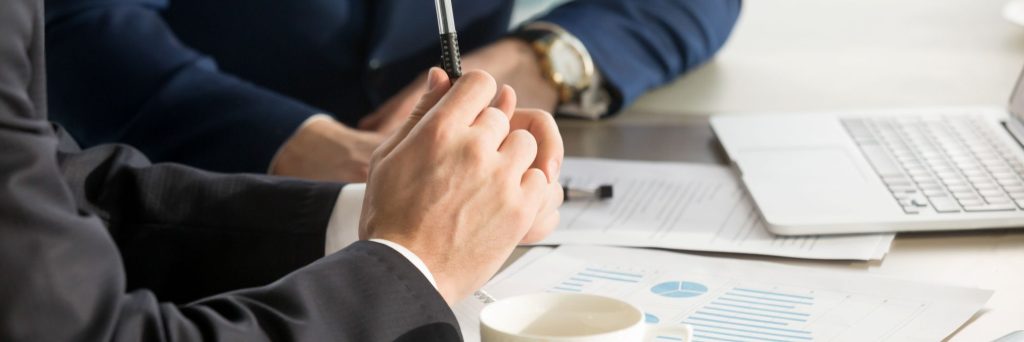 person in suit holding pen above paperwork