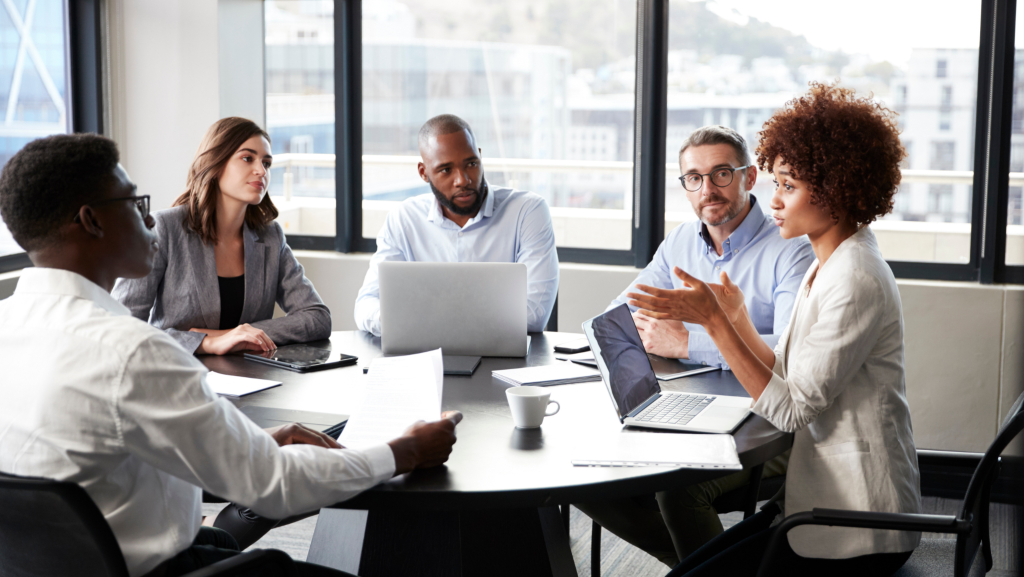 Office workers surrounding a table talking with laptops taking