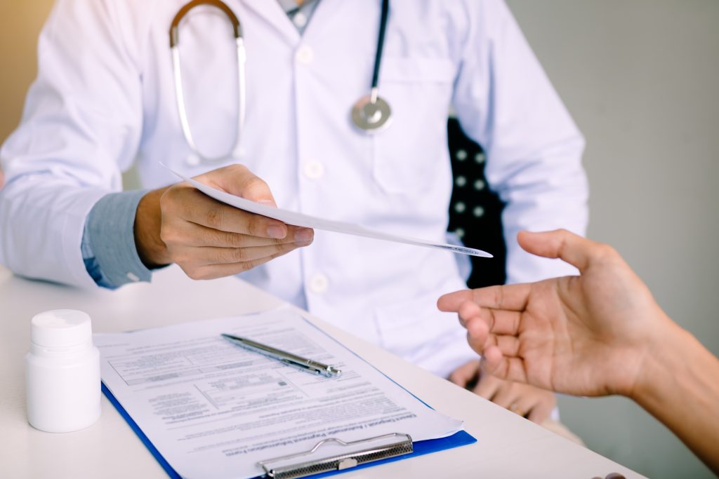 Male doctor handing a prescription to the patient.