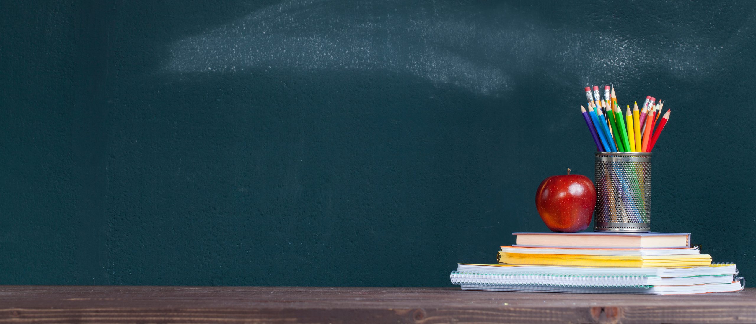 Pencil tray and an apple on notebooks on school teacher's desk